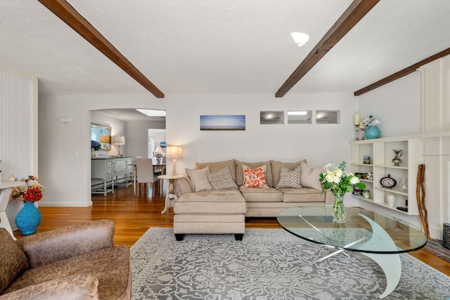 living area featuring beam ceiling, wood finished floors, arched walkways, and baseboards