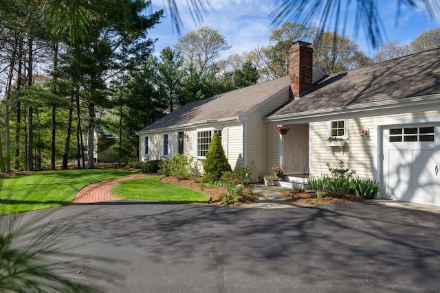 view of front of home featuring an attached garage, a chimney, driveway, a front yard, and roof with shingles