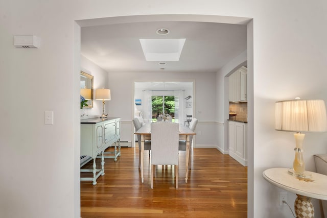 dining space with light wood-style flooring, a skylight, and a baseboard heating unit