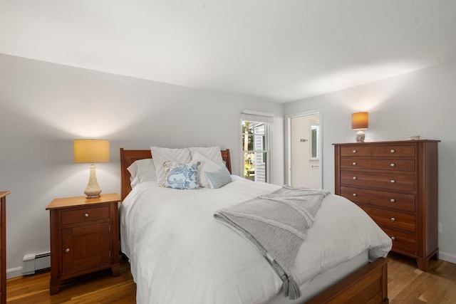 bedroom with wood finished floors, a baseboard radiator, ensuite bathroom, and baseboards