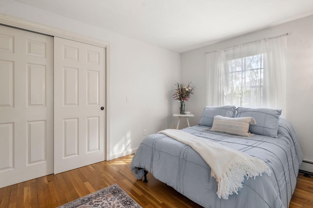 bedroom with wood finished floors, a closet, and baseboard heating
