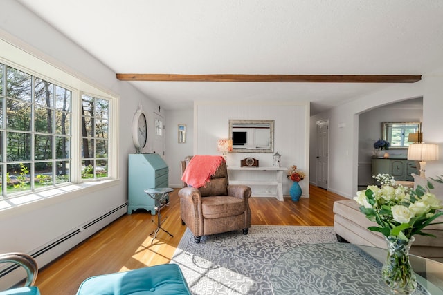 living room featuring beam ceiling, healthy amount of natural light, a baseboard heating unit, wood finished floors, and baseboards