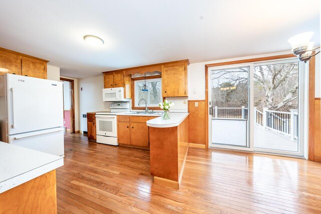 kitchen with light wood-style flooring, a peninsula, white appliances, a sink, and light countertops