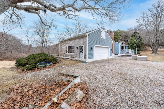 view of home's exterior featuring a garage, a chimney, and gravel driveway