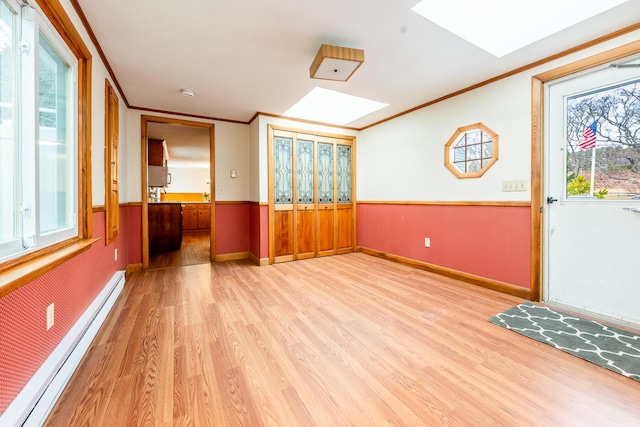 interior space with a baseboard radiator, a wainscoted wall, a skylight, ornamental molding, and light wood finished floors