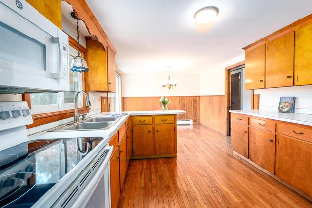 kitchen with a wainscoted wall, baseboard heating, brown cabinetry, a sink, and white appliances