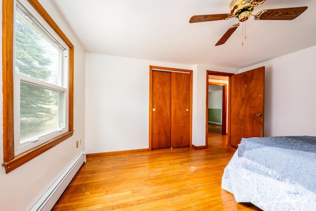 bedroom featuring a baseboard heating unit, a ceiling fan, baseboards, light wood-style floors, and a closet