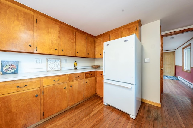 kitchen with brown cabinets, light countertops, light wood-style flooring, freestanding refrigerator, and baseboards