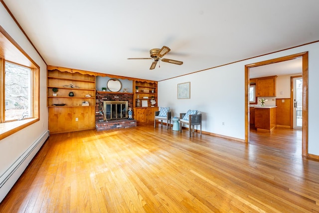 unfurnished living room featuring a baseboard heating unit, light wood-type flooring, a brick fireplace, and plenty of natural light