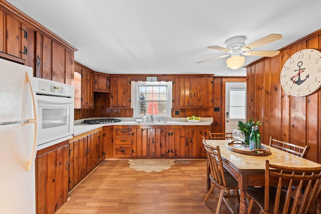 kitchen featuring white appliances, wooden walls, ceiling fan, and light wood-type flooring