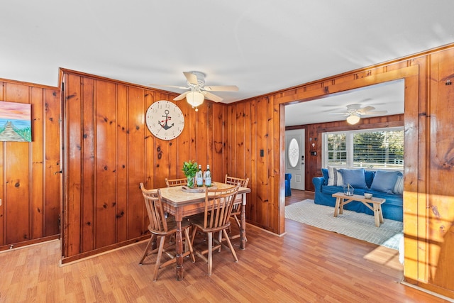 dining room featuring ceiling fan, light wood-type flooring, and wood walls