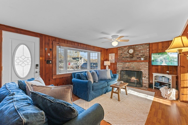 living room featuring a brick fireplace, light hardwood / wood-style floors, ceiling fan, and wood walls