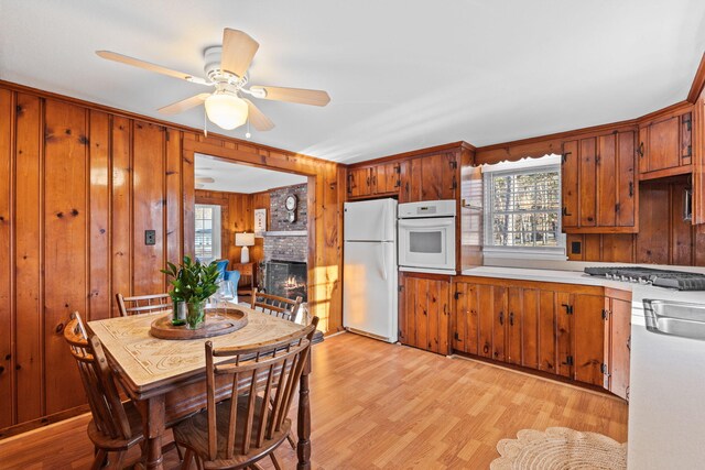 kitchen with a brick fireplace, a wealth of natural light, white appliances, and light hardwood / wood-style floors