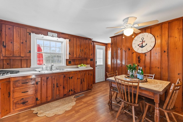 kitchen featuring ceiling fan, light hardwood / wood-style floors, sink, and wood walls