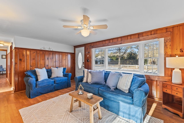 living room featuring ceiling fan, wooden walls, and light hardwood / wood-style floors