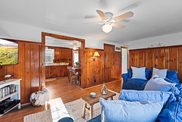 living room featuring ceiling fan, hardwood / wood-style floors, and wood walls