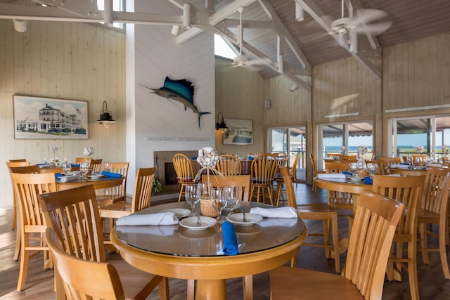 dining room with wood-type flooring, high vaulted ceiling, beam ceiling, ceiling fan, and wood walls