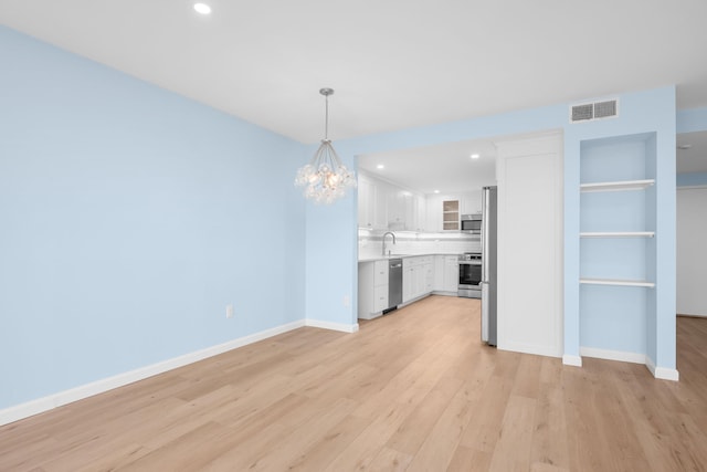 kitchen with light hardwood / wood-style flooring, white cabinets, an inviting chandelier, decorative backsplash, and stainless steel appliances