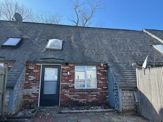 exterior space featuring brick siding, a shingled roof, and fence