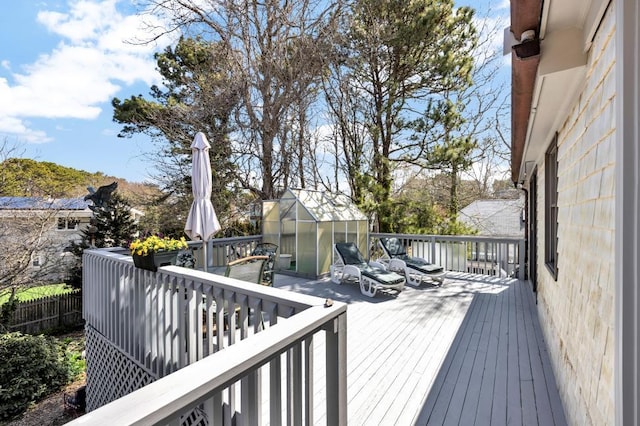 wooden deck featuring a greenhouse, an outbuilding, and outdoor dining space
