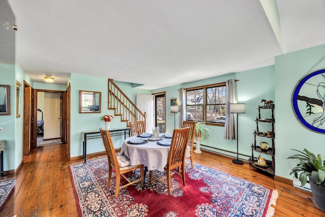 dining space with stairway, wood-type flooring, a baseboard radiator, and baseboards