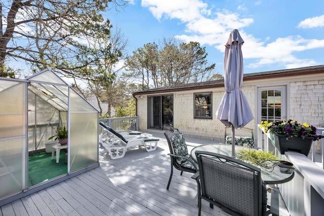 wooden deck with a greenhouse and outdoor dining space