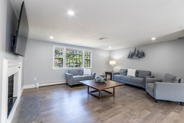 living room with hardwood / wood-style floors, a baseboard heating unit, a textured ceiling, and a fireplace