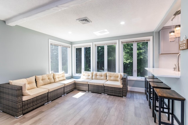 living room with a textured ceiling, beamed ceiling, and light hardwood / wood-style flooring