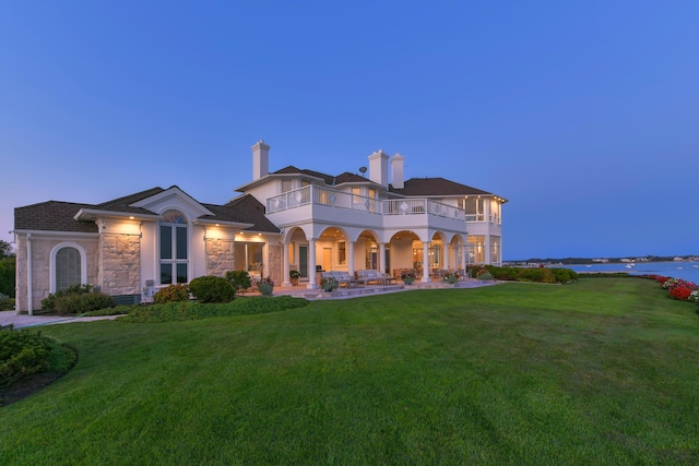 view of front of house featuring a balcony, a lawn, and a water view