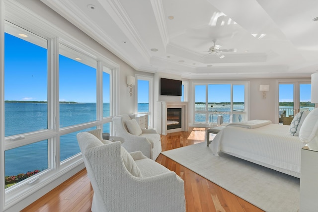 bedroom with light wood-type flooring, multiple windows, a tray ceiling, and ornamental molding