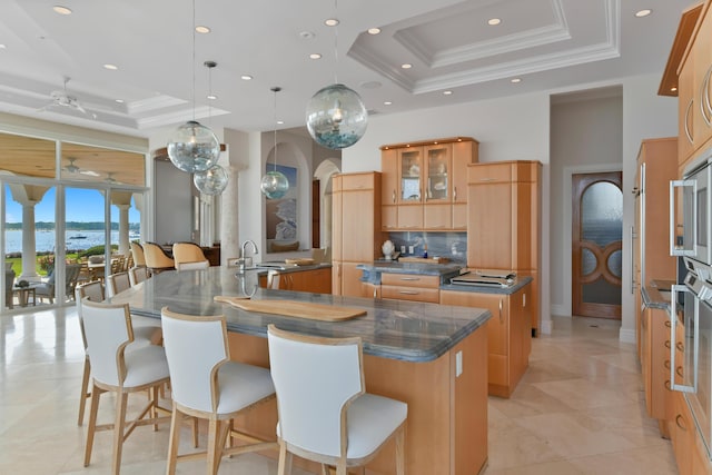 kitchen with crown molding, hanging light fixtures, a large island, a kitchen breakfast bar, and a raised ceiling