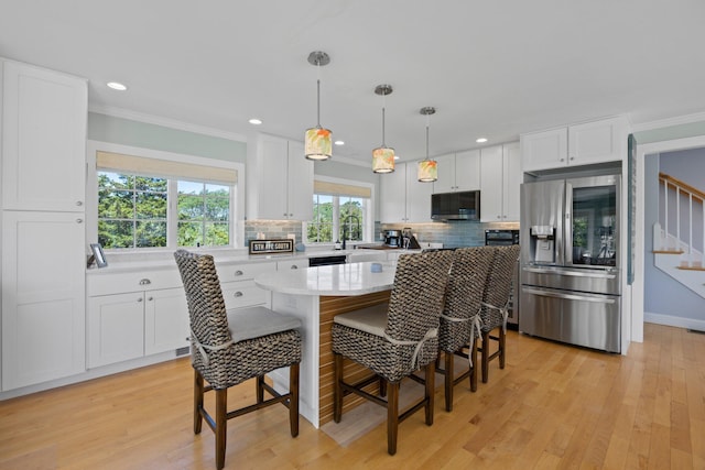 kitchen featuring light hardwood / wood-style floors, appliances with stainless steel finishes, white cabinetry, hanging light fixtures, and a kitchen island