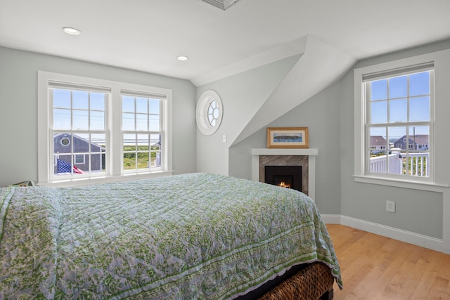 bedroom featuring light hardwood / wood-style flooring, lofted ceiling, and a fireplace