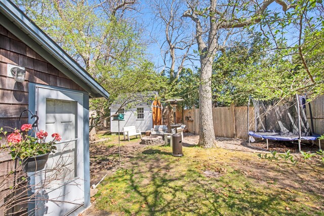 view of yard with an outdoor fire pit, a storage unit, and a trampoline