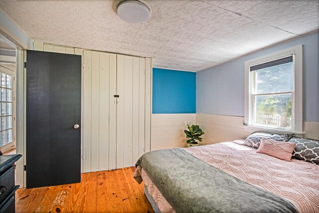 bedroom featuring wood-type flooring, wooden walls, and a textured ceiling