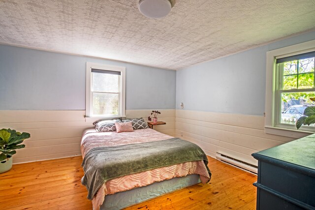 bedroom featuring a textured ceiling, baseboard heating, and light hardwood / wood-style flooring