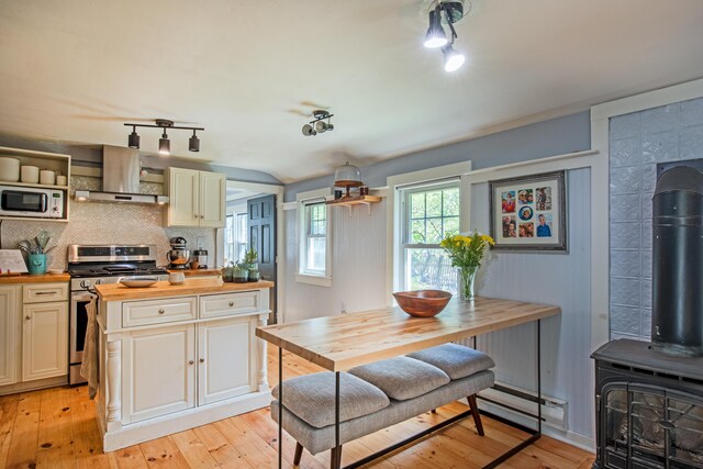 kitchen with stainless steel gas range, wood counters, a wood stove, backsplash, and light wood-type flooring