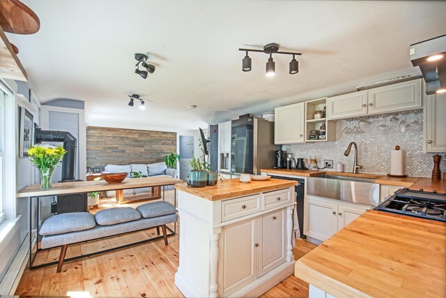 kitchen with a center island, butcher block counters, white cabinetry, sink, and backsplash