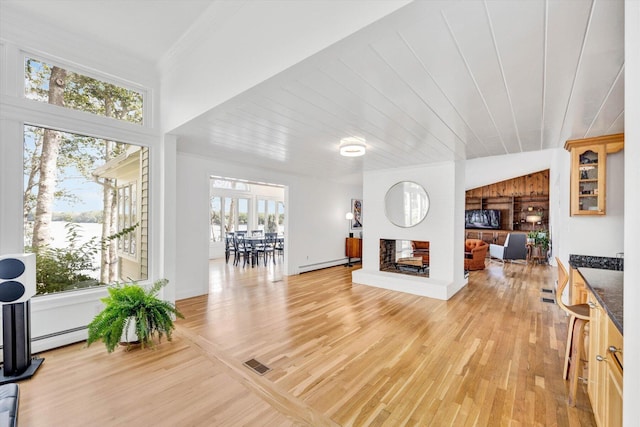 living room with baseboard heating, crown molding, a brick fireplace, and light wood-type flooring