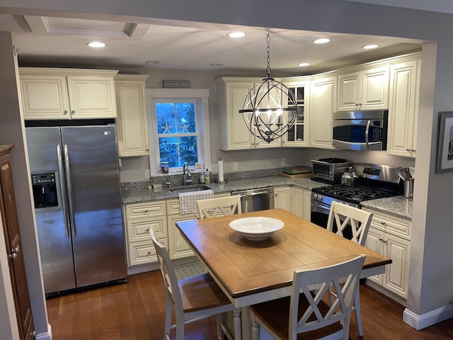 kitchen with light stone countertops, appliances with stainless steel finishes, decorative light fixtures, a raised ceiling, and dark wood-type flooring