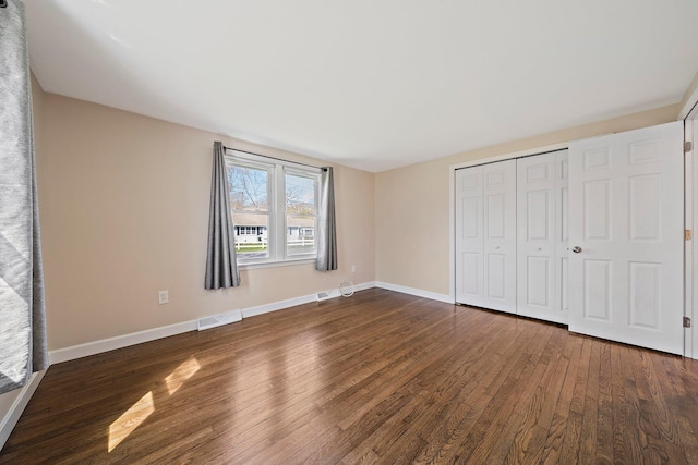unfurnished bedroom with baseboards, dark wood finished floors, visible vents, and a closet