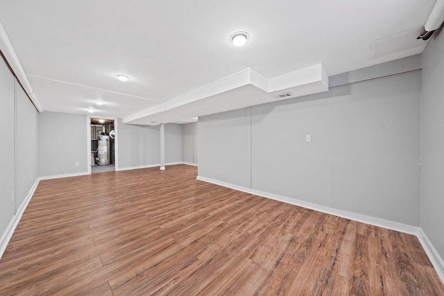 finished below grade area featuring visible vents, baseboards, gas water heater, and wood finished floors