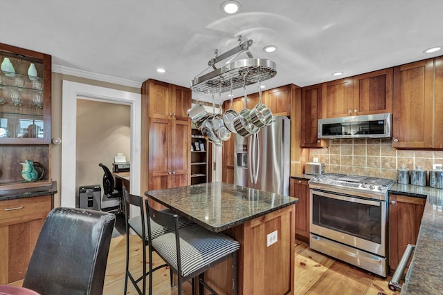 kitchen featuring light hardwood / wood-style flooring, dark stone countertops, ornamental molding, a kitchen island, and stainless steel appliances