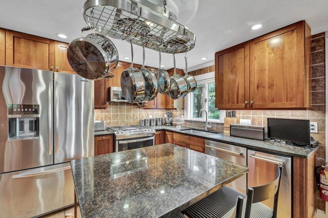 kitchen with appliances with stainless steel finishes, dark stone countertops, decorative backsplash, sink, and a breakfast bar area