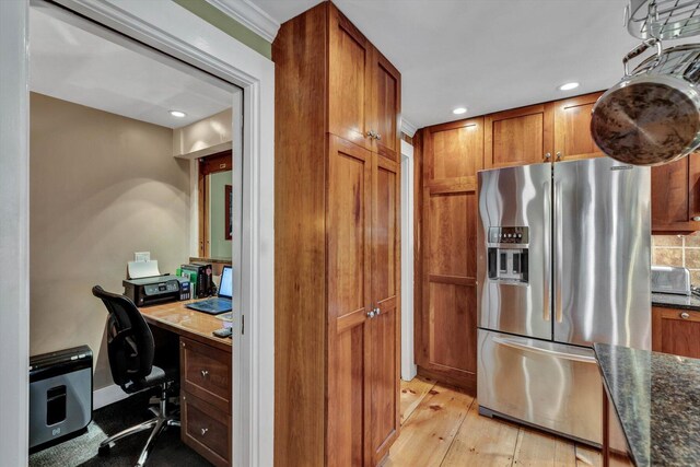 kitchen with crown molding, light hardwood / wood-style floors, backsplash, dark stone counters, and stainless steel fridge