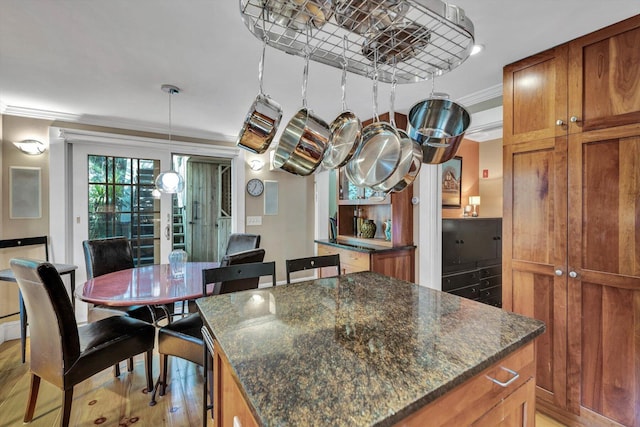 kitchen featuring a kitchen island, dark stone countertops, light hardwood / wood-style flooring, ornamental molding, and pendant lighting