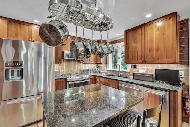 184 Bradford St Unit U1, Provincetown, MA 02657 - kitchen with appliances with stainless steel finishes, brown cabinetry, decorative backsplash, dark stone counters, and recessed lighting