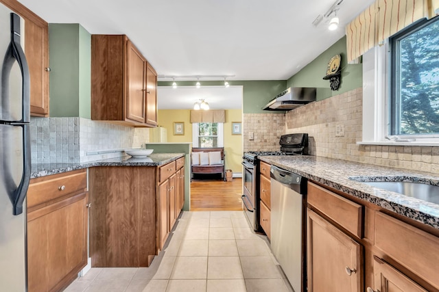 kitchen featuring a healthy amount of sunlight, light tile patterned floors, stainless steel appliances, and dark stone counters