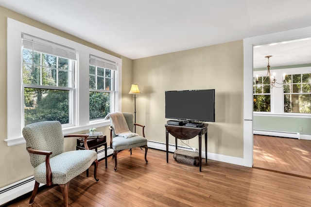 living area with a notable chandelier, hardwood / wood-style flooring, a baseboard radiator, and a healthy amount of sunlight