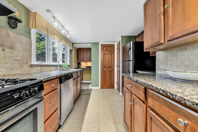 kitchen featuring appliances with stainless steel finishes, stone counters, light tile patterned flooring, backsplash, and sink